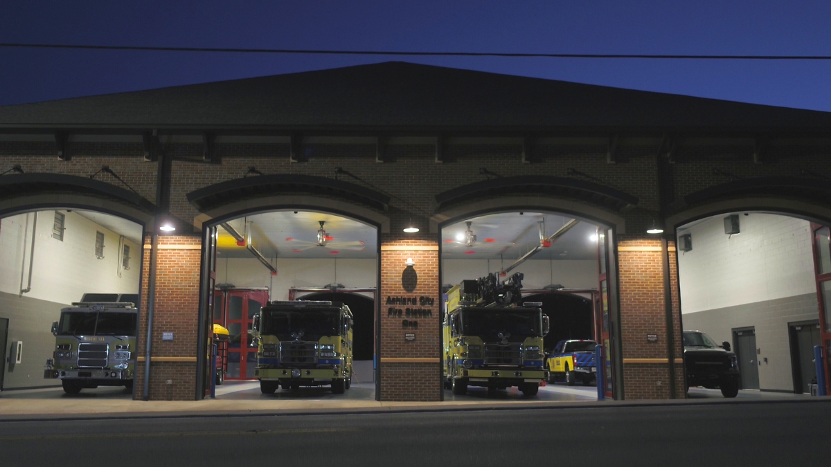Ashland City Fire Department building at dusk with fire trucks and an emergency vehicle inside the open bays