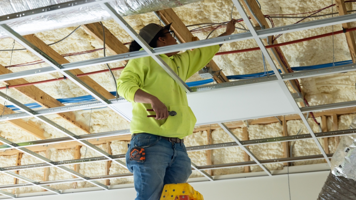 Commercial electrician installing wiring above a suspended ceiling grid
