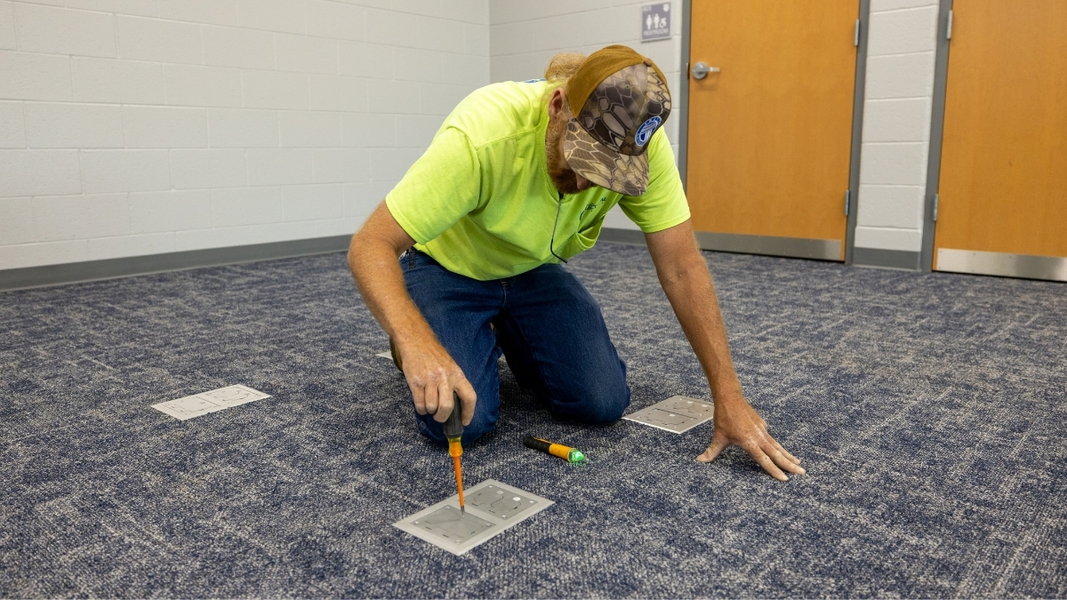 Travis Electrical Service electrician installing a floor outlet in a carpeted commercial space