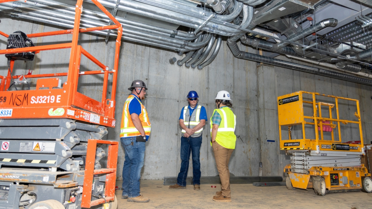 Construction team discussing work beneath installed conduit and ductwork