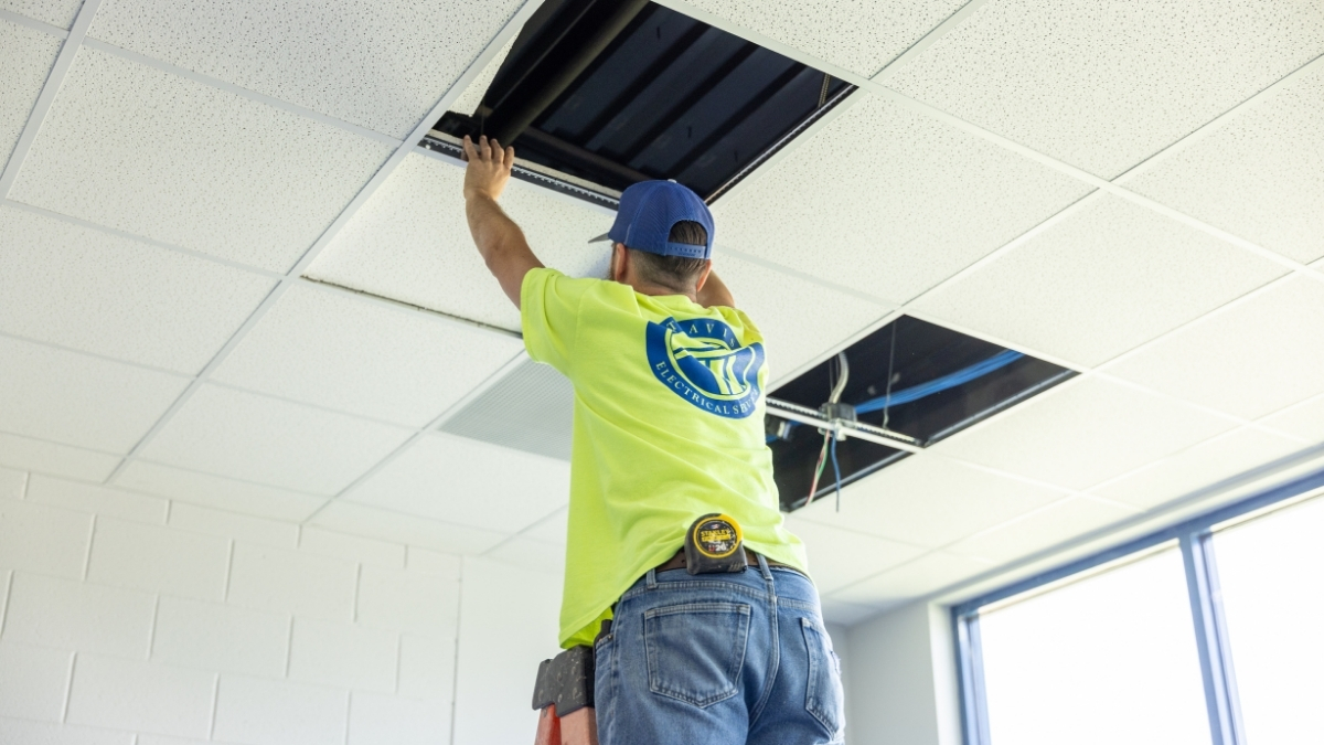 Commercial electrician installing electrical wiring above a suspended ceiling