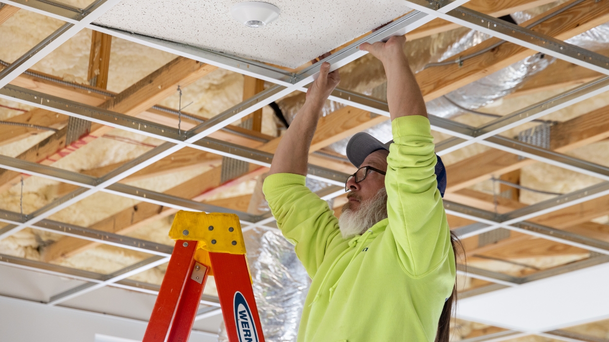 Electrician installing a ceiling tile in a suspended ceiling grid