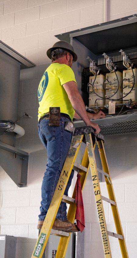 Electrician standing on ladder at commercial facility