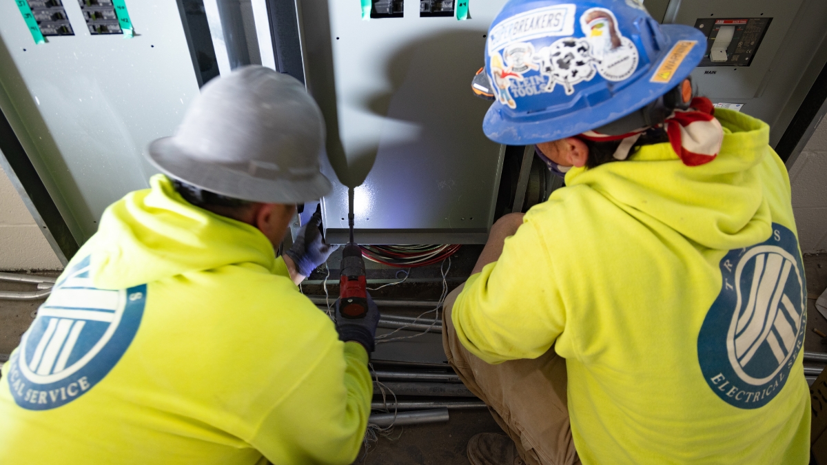 Two commercial electricians wiring an electrical panel at the Wyatt Johnson Subaru construction site