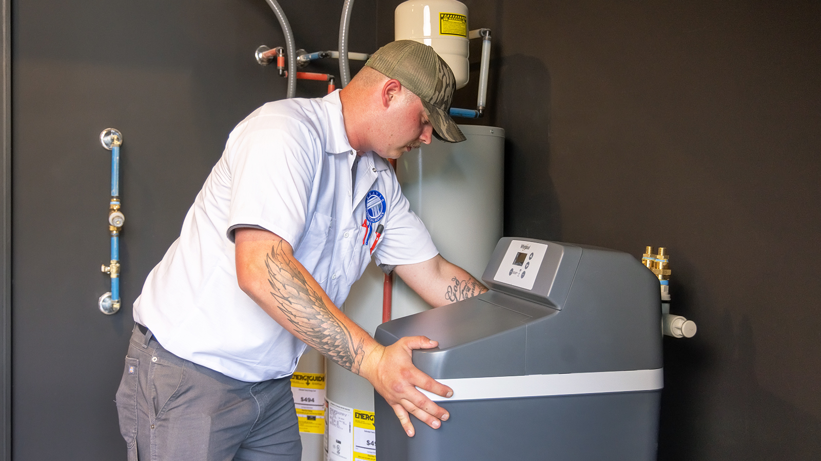 A plumber in a blue uniform adjusts the control panel on a residential water filtration system.