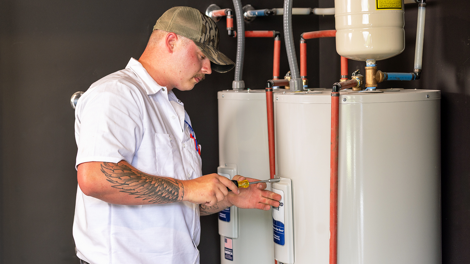 A plumber wearing a blue uniform tightens a panel on a residential water heater during a maintenance service.