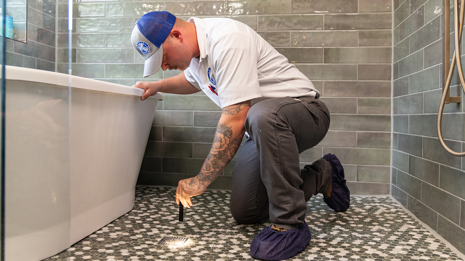 Plumber wearing a blue sweatshirt and cap working on a shower handle.