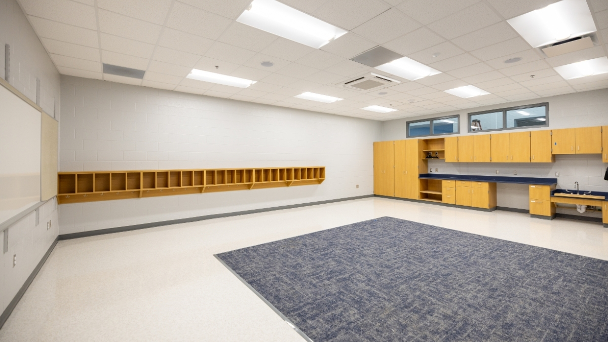 Modern school classroom with wood cabinets, whiteboard and carpeted learning area