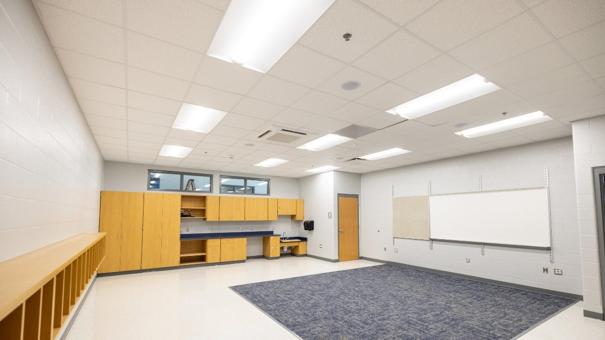 Spacious school classroom with wood cabinets, whiteboard and carpeted instructional area