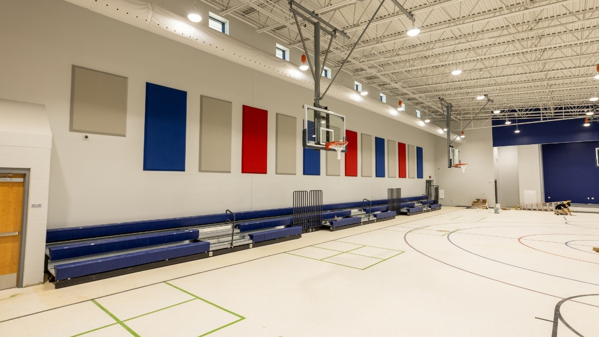 School gymnasium with basketball goals, retractable bleachers and acoustic wall panels