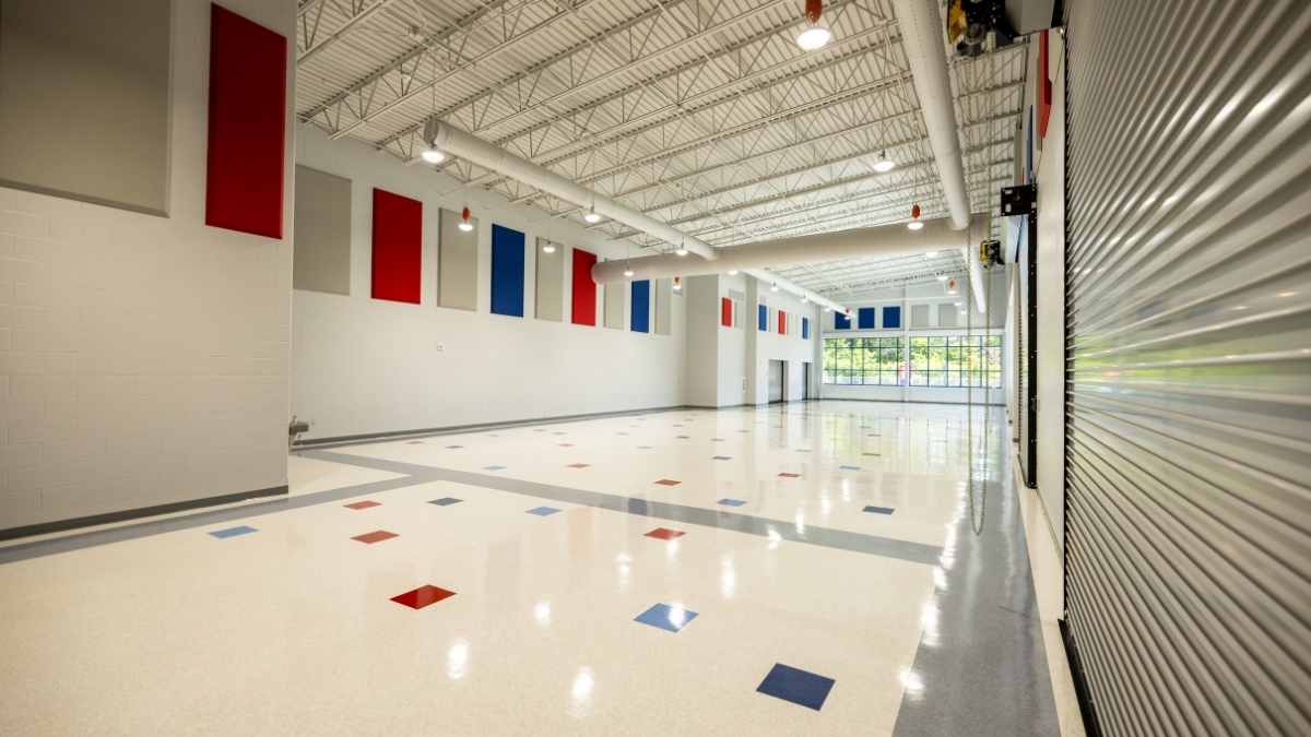 Large school multipurpose room with polished floors, colorful wall panels and natural light