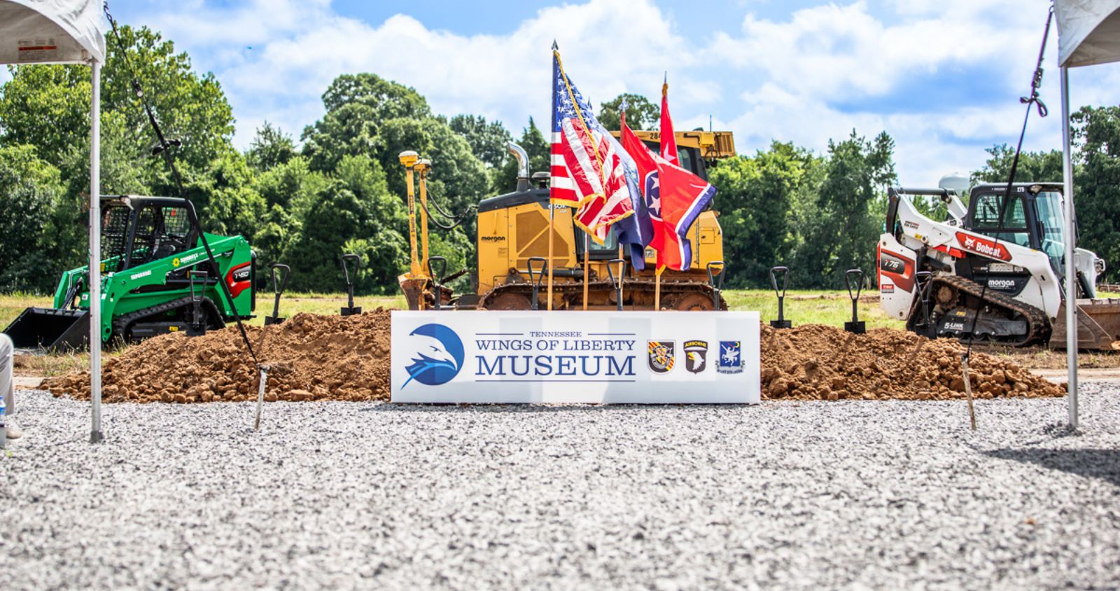 USA Flag and Tennessee flag in pile of dirt with construction vehicle behind and sign that says Tennessee Wings of Liberty Museum